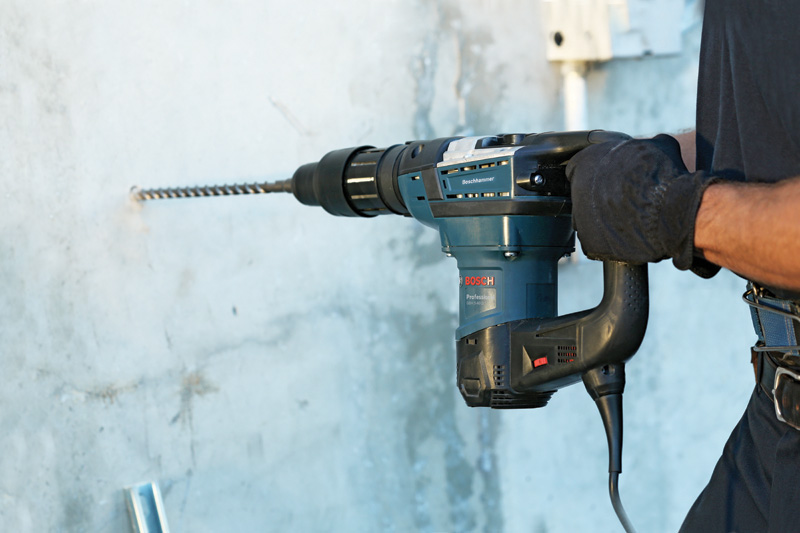 Eine Person mit Schutzausrüstung bohrt mit einem Bohrhammer in Beton. Anwendungsbild