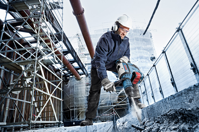 Eine Person mit Schutzausrüstung bedient einen Akku-Bohrhammer auf einer Betonplatte. Anwendungsbild
