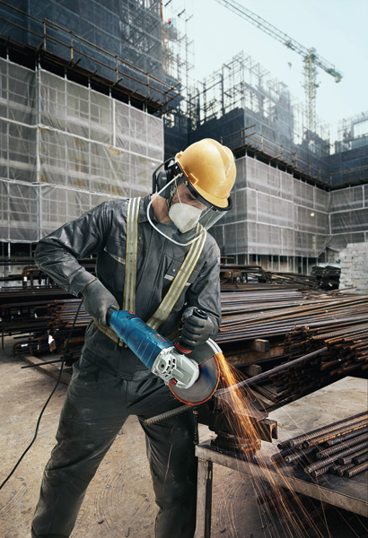 Eine Person mit Sicherheitsausrüstung schleift auf einer Baustelle Metallstangen mit einem Winkelschleifer. Anwendungsbild