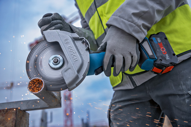 Eine Person mit Sicherheitsausrüstung schneidet Metallrohre mit einem Akku-Winkelschleifer. Anwendungsbild