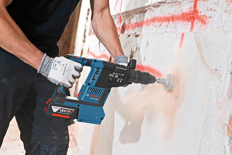 Eine Person mit Schutzausrüstung bohrt mit einem Akku-Bohrhammer in eine Betonwand. Anwendungsbild