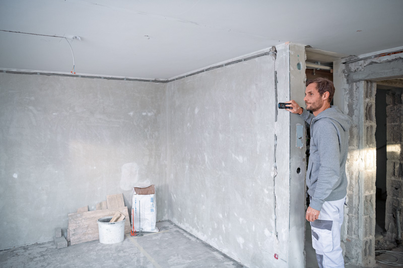Eine Person misst mit einem Lasermessgerät eine Wand in einem im Bau befindlichen Gebäude. Anwendungsbild