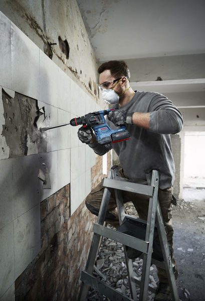 Eine Person mit Schutzausrüstung entfernt Wandfliesen mit einem Bohrhammer. Anwendungsbild