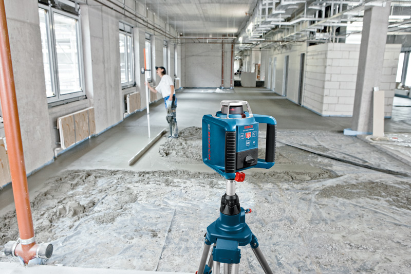 Eine Person mit Sicherheitsausrüstung überprüft beim Nivellieren von Beton ein Lasernivelliergerät auf einem Stativ. Anwendungsbild