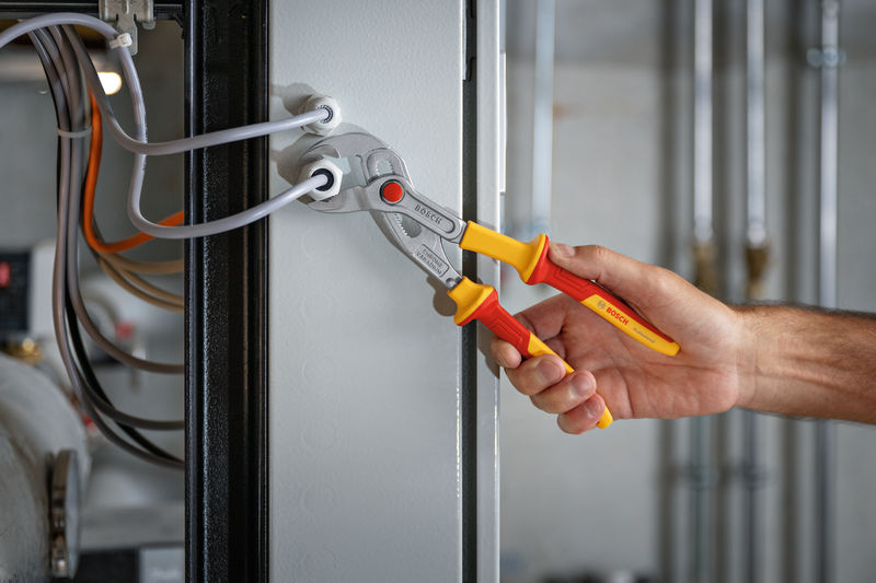 Eine Person verwendet eine isolierte Zange, um an der elektrischen Verkabelung in einem Panel zu arbeiten. Anwendungsbild
