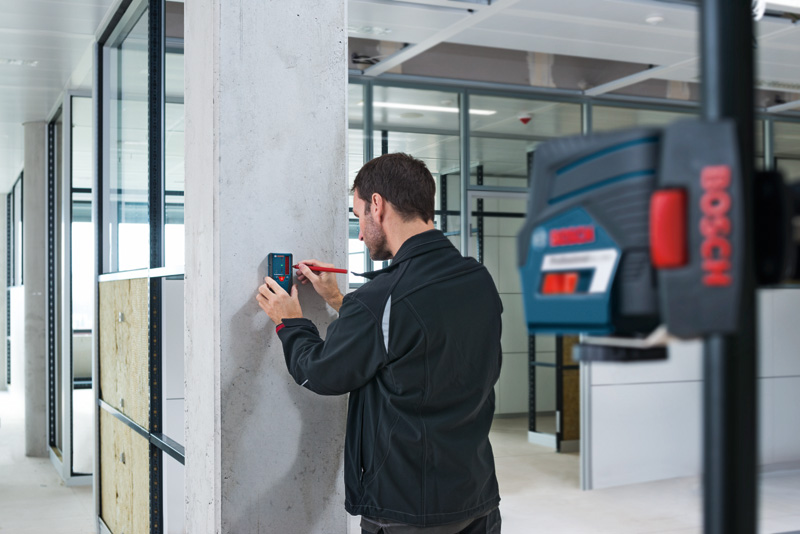 Person markiert in einem modernen Büroraum einen Betonpfeiler mit einem Laserempfänger. Anwendungsbild
