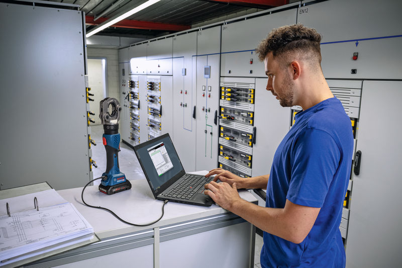 In einem elektrischen Kontrollraum bedient eine Person einen Laptop, der an ein kabelloses hydraulisches Crimpwerkzeug angeschlossen ist. Anwendungsbild