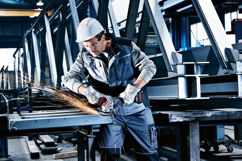 Eine Person mit Schutzausrüstung schleift Metallträger mit einem Akku-Winkelschleifer. Anwendungsbild