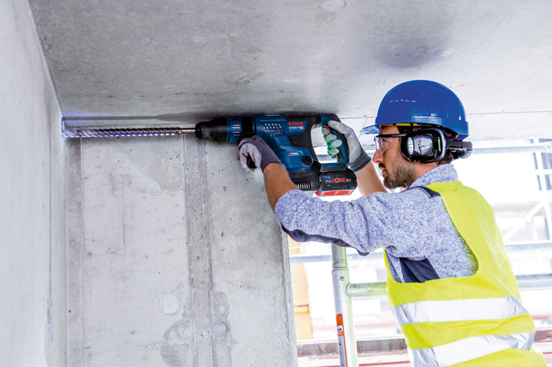 Eine Person mit Schutzausrüstung bohrt mit einem Bohrhammer in eine Betondecke. Anwendungsbild