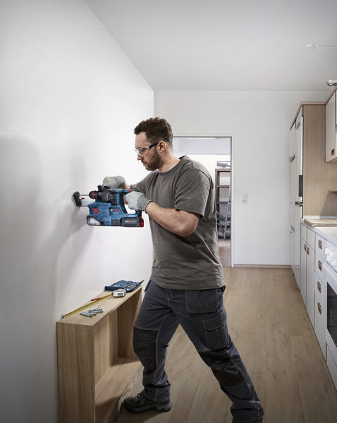 Eine Person mit Sicherheitsausrüstung bohrt in eine Wand in einer Küche. Anwendungsbild