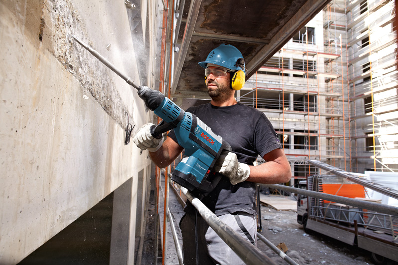 Eine Person mit Sicherheitsausrüstung bohrt auf einer Baustelle in eine Betonwand. Anwendungsbild