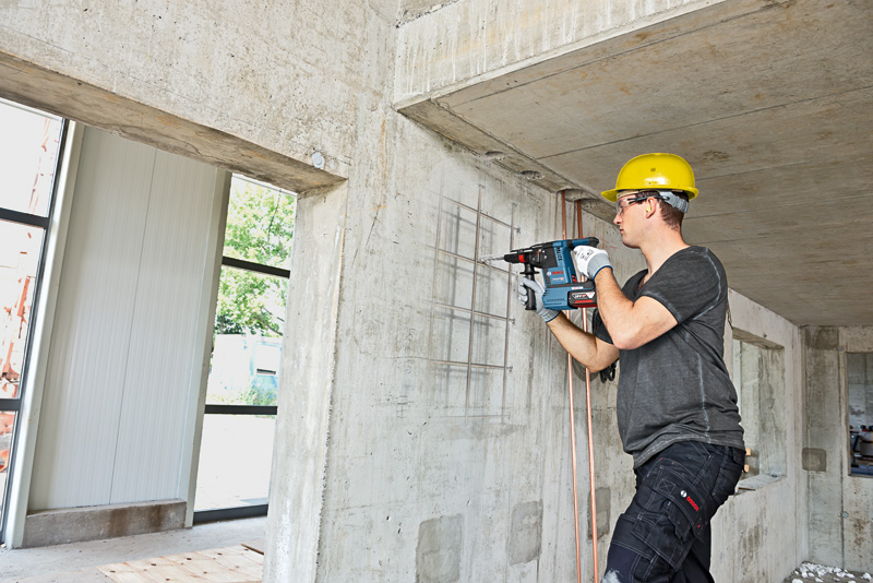 Eine Person mit Schutzausrüstung bohrt mit einem Bohrhammer in eine Betonwand. Anwendungsbild