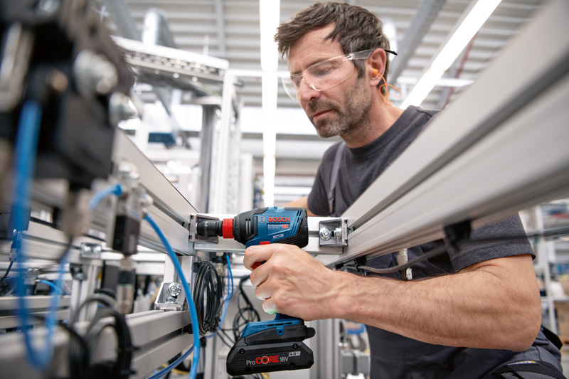 Eine Person mit Schutzausrüstung befestigt mit einer Akku-Bohrmaschine ein Metallgerüst. Anwendungsbild