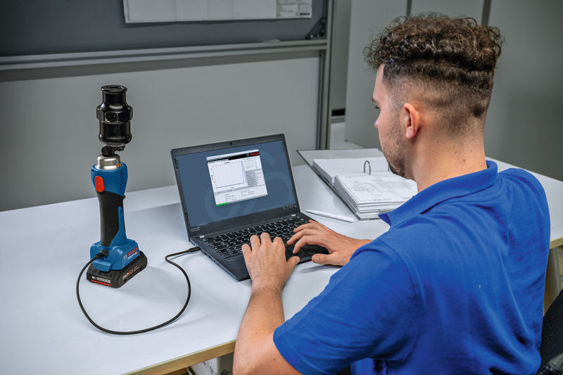 Eine Person verbindet ein kabelloses hydraulisches Stanzwerkzeug mit einem Laptop an einem Schreibtisch. Anwendungsbild
