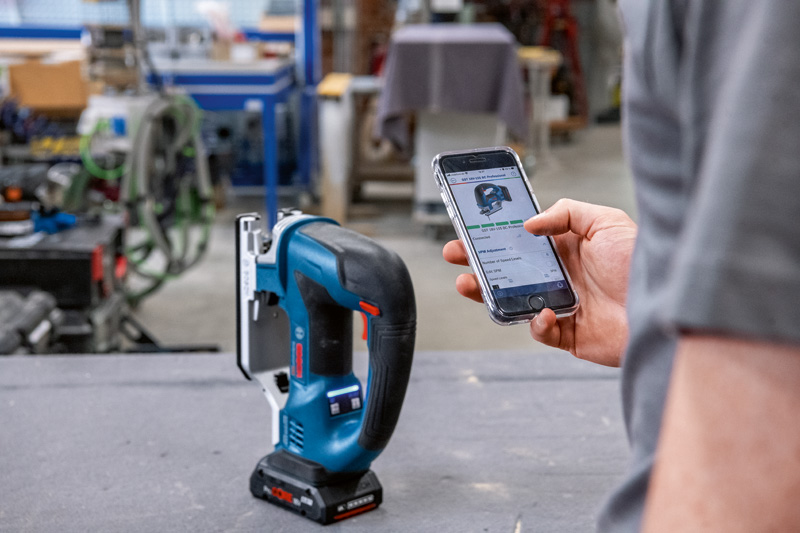 Eine Person stellt in einer Werkstatt per Smartphone eine Akku-Stichsäge ein. Anwendungsbild