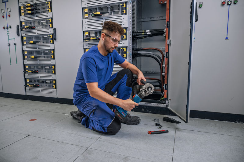 Eine Person mit Sicherheitsausrüstung crimpt ein Kabel mit einem kabellosen Hydraulikwerkzeug. Anwendungsbild