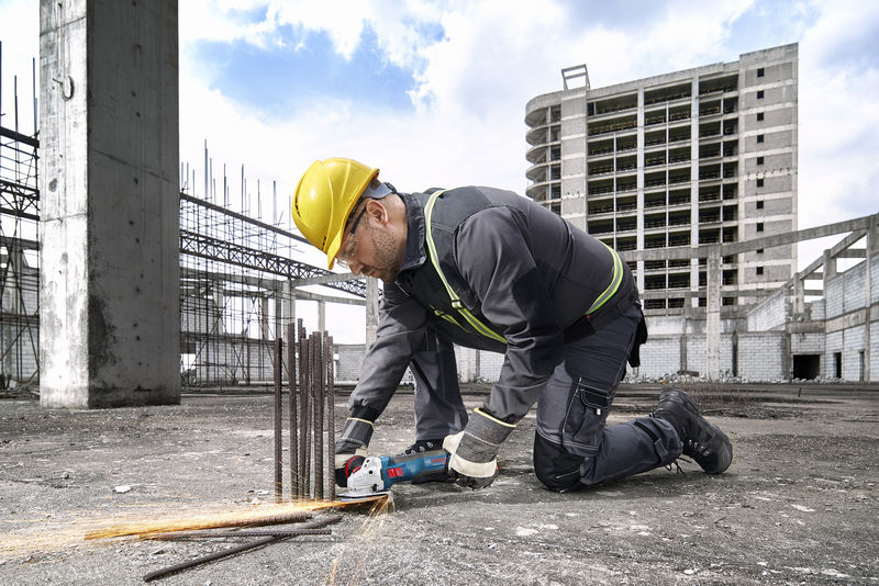 Eine Person mit Sicherheitsausrüstung schneidet auf einer Baustelle Bewehrungsstahl mit einem Elektrowerkzeug. Anwendungsbild