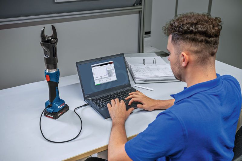 Eine Person verbindet ein kabelloses hydraulisches Schneidwerkzeug zur Datenanalyse mit einem Laptop. Anwendungsbild