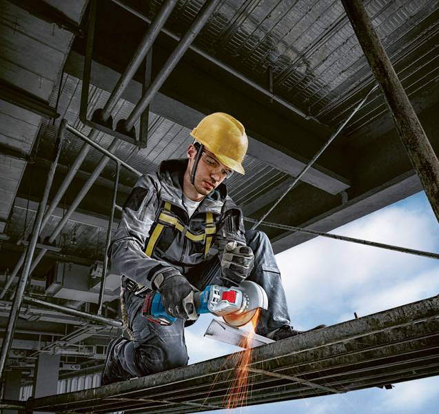 Eine Person mit Schutzausrüstung schneidet mit einem Winkelschleifer Metallträger. Anwendungsbild