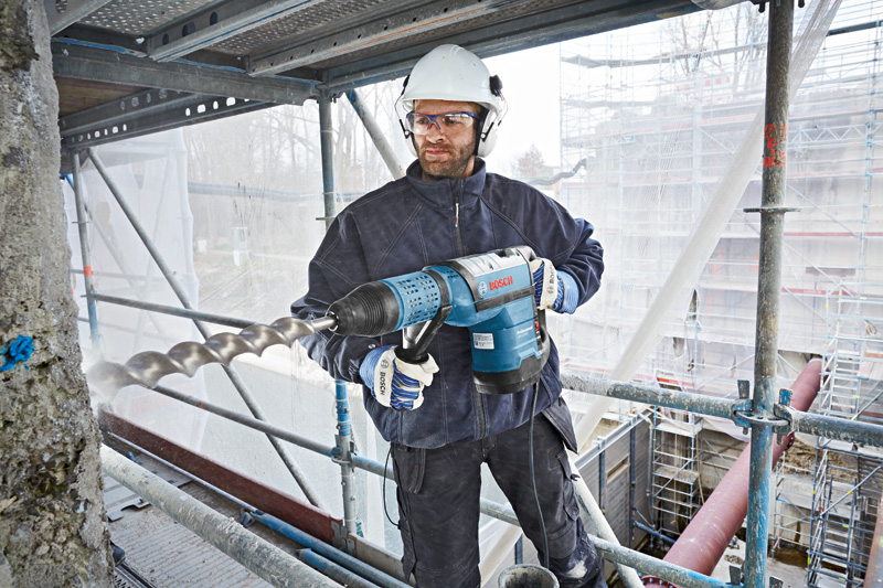 Eine Person mit Schutzausrüstung bohrt mit einem großen Bohrhammer in Beton. Anwendungsbild