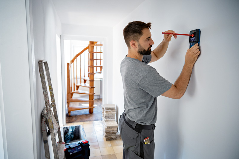Person, die eine Wand mit einem Bleistift markiert und dabei ein Detektorwerkzeug verwendet. Anwendungsbild