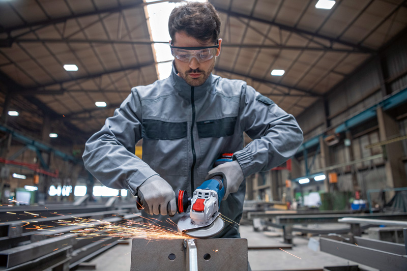 Eine Person mit Schutzausrüstung schleift Metall mit einem Akku-Winkelschleifer. Anwendungsbild