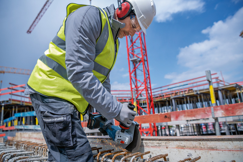 Eine Person mit Sicherheitsausrüstung schneidet auf einer Baustelle Bewehrungsstahl mit einem Akku-Winkelschleifer. Anwendungsbild