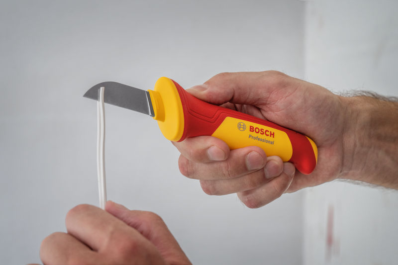 Eine Person verwendet ein isoliertes Universalmesser, um elektrische Leitungen zu durchtrennen. Anwendungsbild