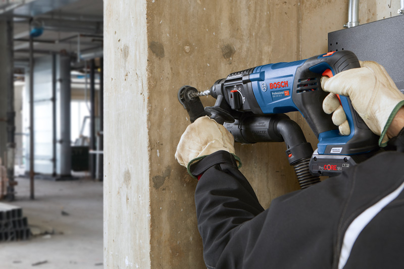 Eine Person mit Schutzausrüstung bohrt mit einem Akku-Bohrhammer in eine Betonwand. Anwendungsbild