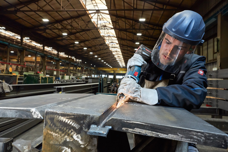 Eine Person mit Sicherheitsausrüstung schleift in einer Fabrik Metall mit einem Elektrowerkzeug. Anwendungsbild