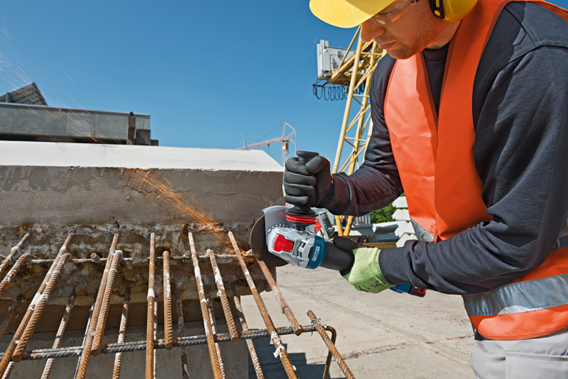 Eine Person mit Sicherheitsausrüstung schleift auf einer Baustelle Bewehrungsstahl. Anwendungsbild