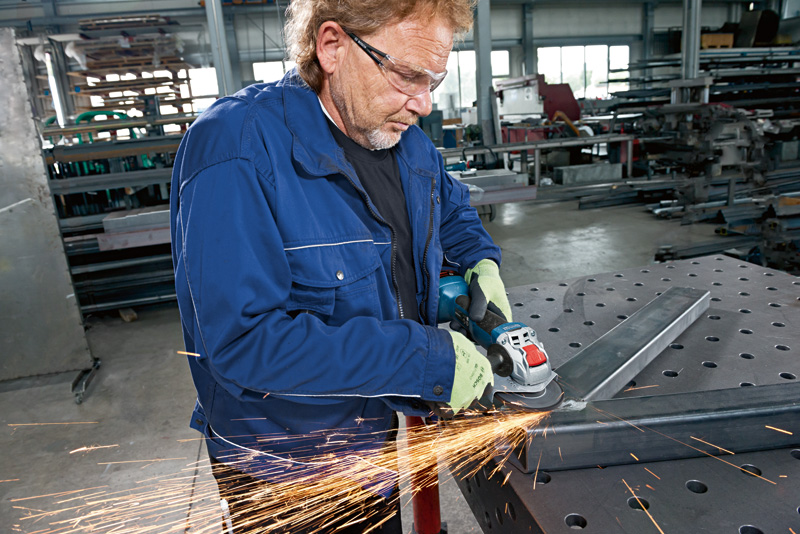 Eine Person mit Schutzausrüstung schleift Metall mit einem Akku-Winkelschleifer. Anwendungsbild