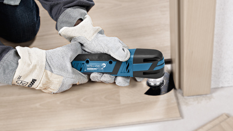 Eine Person mit Schutzausrüstung schneidet Laminatböden mit einem Akku-Multischneider. Anwendungsbild