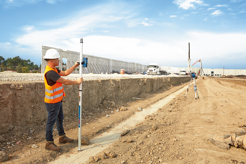 Eine Person mit Sicherheitsausrüstung verwendet auf einer Baustelle einen Laserempfänger. Anwendungsbild