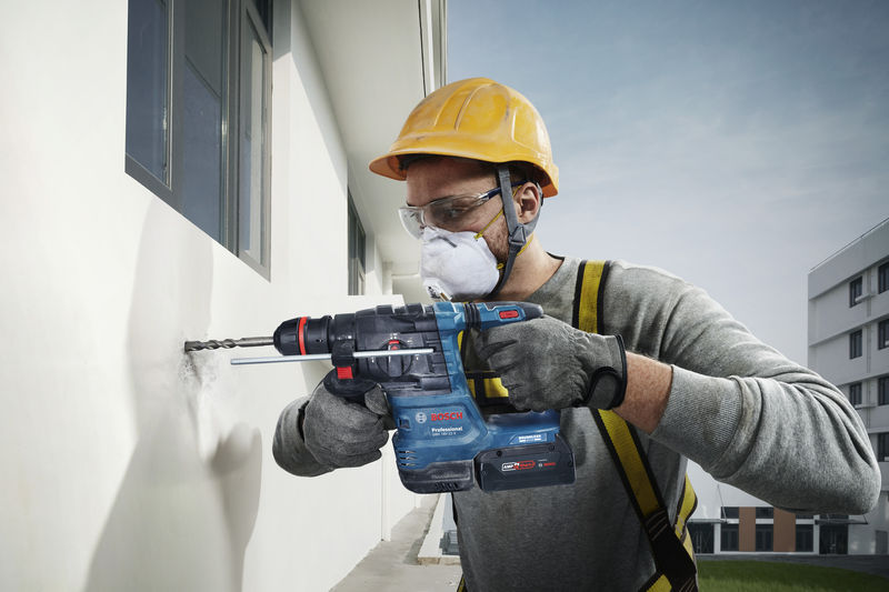 Person mit Schutzausrüstung bohrt mit Akku-Bohrhammer in eine Wand. Anwendungsbild