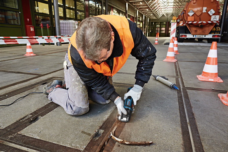 Eine Person mit Sicherheitsausrüstung entfernt mit einem Multischneider Material aus einer Betonfuge. Anwendungsbild