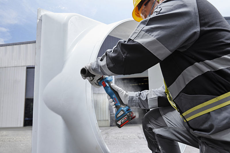 Eine Person mit Schutzausrüstung schleift mit einem Akku-Winkelschleifer ein großes Metallrohr. Anwendungsbild