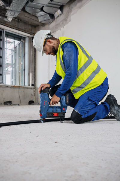 Eine Person mit Sicherheitsausrüstung installiert auf einer Baustelle ein Kabel mit einem Akku-Nagler. Anwendungsbild