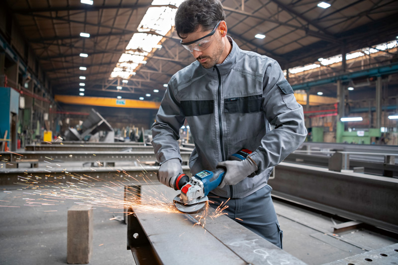 Eine Person mit Schutzausrüstung schleift in einer industriellen Umgebung Metall und erzeugt dabei Funken. Anwendungsbild