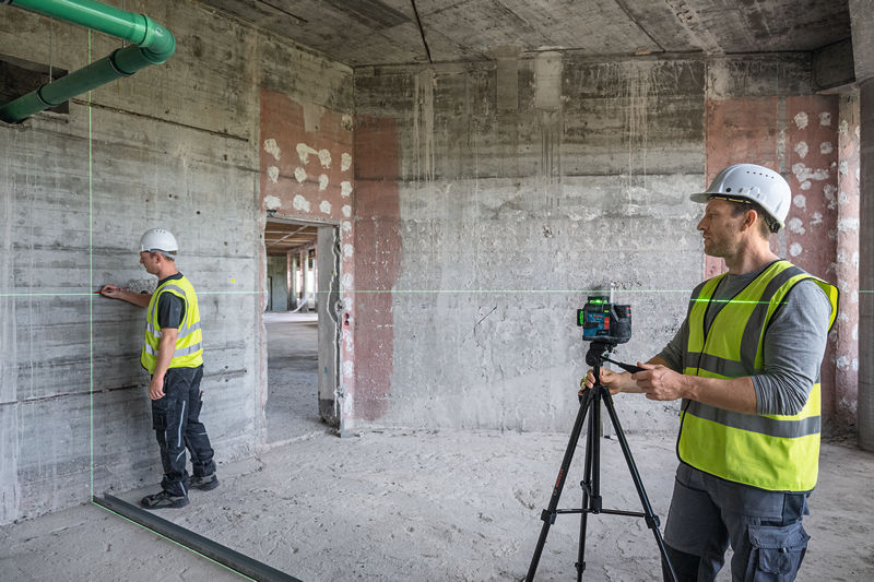 Zwei Arbeiter in Sicherheitsausrüstung verwenden auf einer Baustelle ein Lasernivelliergerät. Anwendungsbild