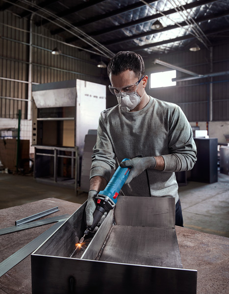 Eine Person mit Sicherheitsausrüstung schleift Metall in einer Industriewerkstatt. Anwendungsbild
