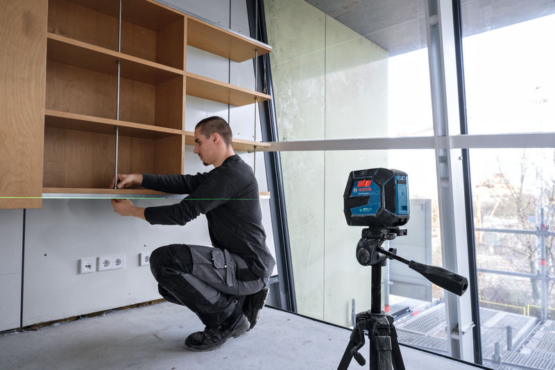 Eine Person installiert ein Regal und verwendet dabei ein Lasernivelliergerät, um es genau auszurichten. Anwendungsbild