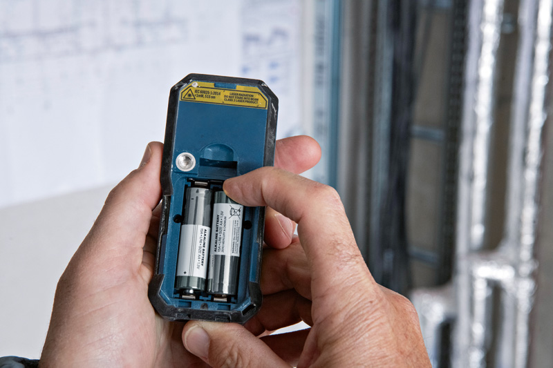 Person legt Batterien in die Rückseite eines Lasermessgeräts ein. Anwendungsbild