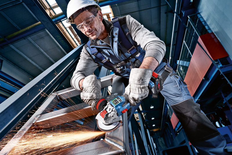 Eine Person mit Schutzausrüstung schleift mit einem Elektrowerkzeug einen Metallträger, wobei Funken entstehen. Anwendungsbild