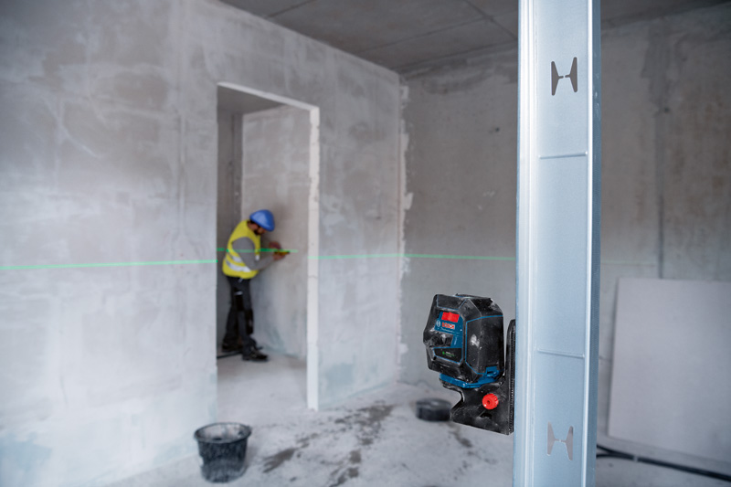 Eine Person mit Sicherheitsausrüstung überprüft die Ausrichtung mit einem Lasernivelliergerät in einem im Bau befindlichen Raum. Anwendungsbild