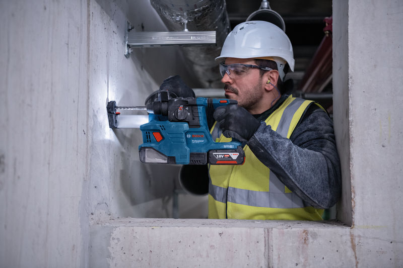 Eine Person mit Schutzausrüstung bohrt mit einem Bohrhammer in eine Betonwand. Anwendungsbild