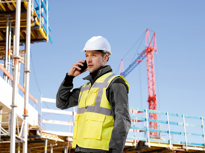 Eine Person mit Sicherheitsausrüstung telefoniert auf einer Baustelle. Anwendungsbild