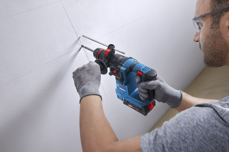 Eine Person mit Schutzausrüstung bohrt mit einem Akku-Bohrhammer ein Loch in eine markierte Wand. Anwendungsbild