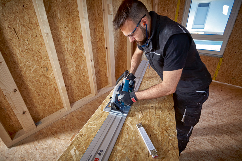 Eine Person mit Sicherheitsausrüstung verwendet eine Kreissäge mit Führungsschiene, um Holz zu schneiden. Anwendungsbild