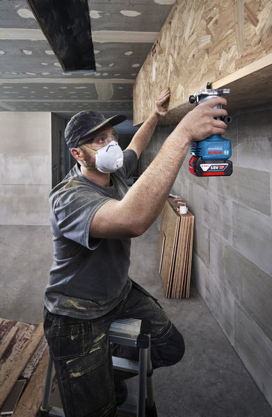 Eine Person mit Schutzausrüstung bedient eine Oberfräse auf einem Holzregal. Anwendungsbild